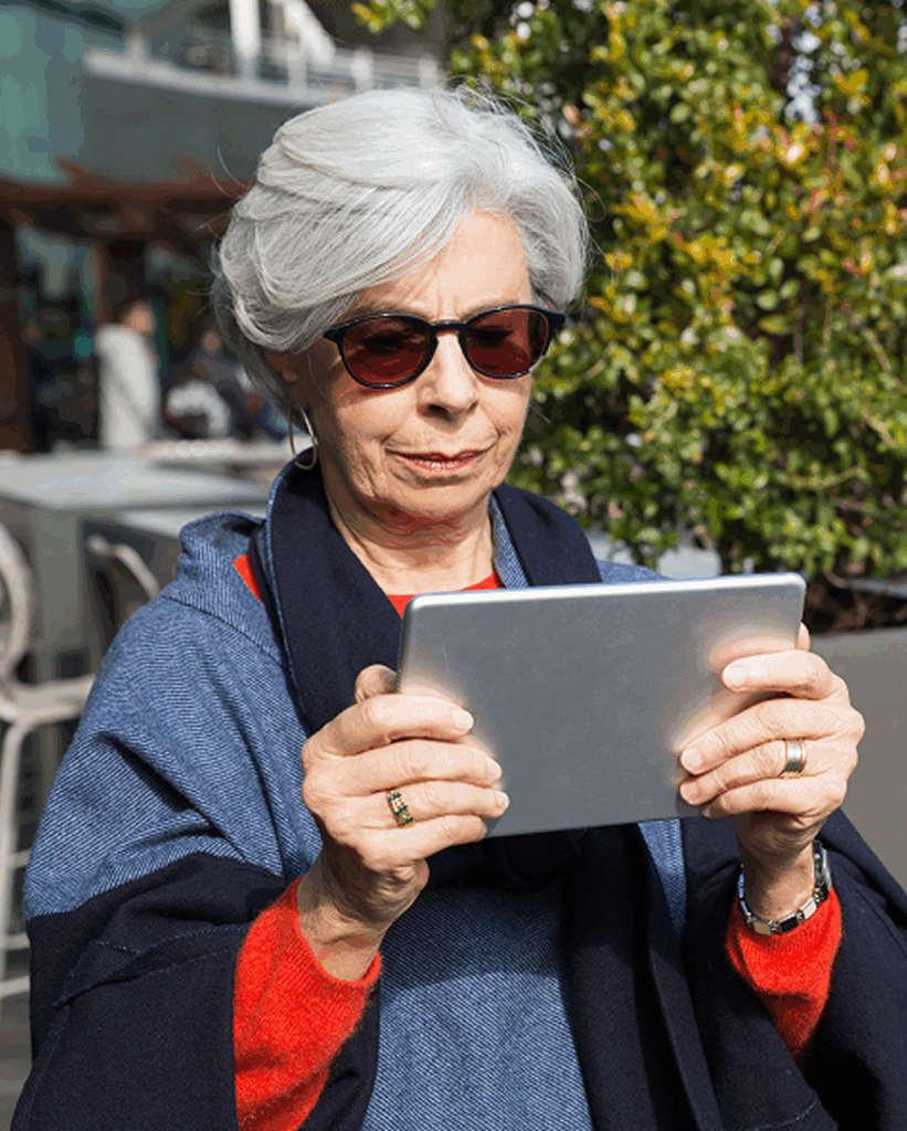 Dona gran amb ulleres fosques utilitzant una tauleta digital a l’aire lliure.
